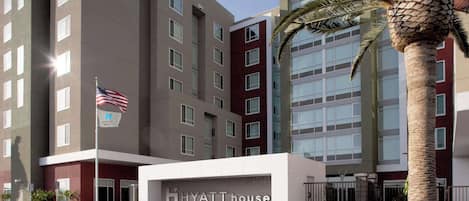 Un hotel de varios pisos con un llamativo letrero de 'Hyatt House', una bandera y una palmera.