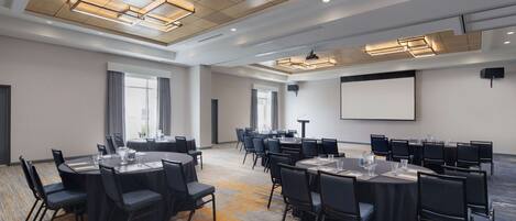 Une salle de conférence équipée de plusieurs tables et chaises, d’un projecteur et d’un écran mural.