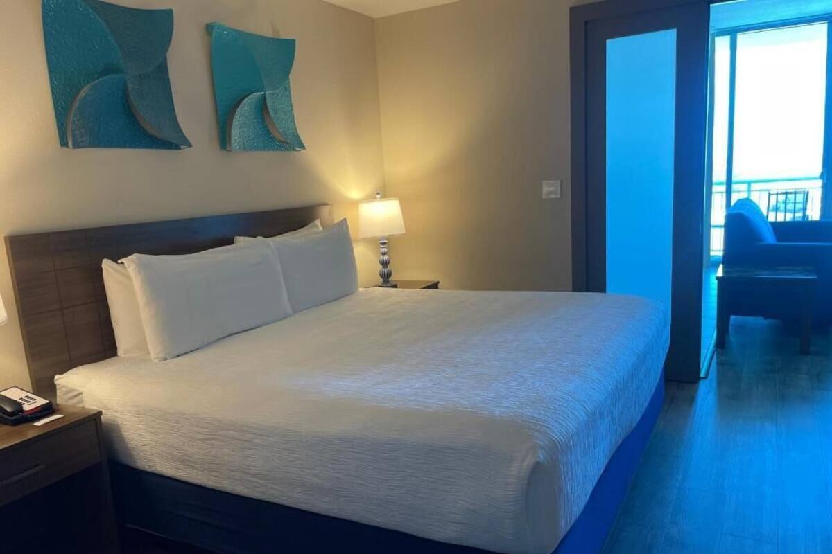 A hotel room with a large bed, a bedside lamp, a phone on the nightstand, and abstract wall art.