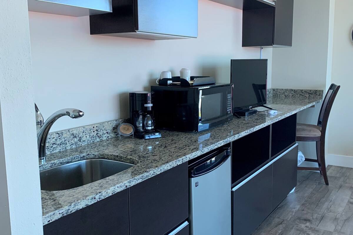 A modern kitchen with dark cabinetry, a granite countertop, a built-in dishwasher, and a microwave.