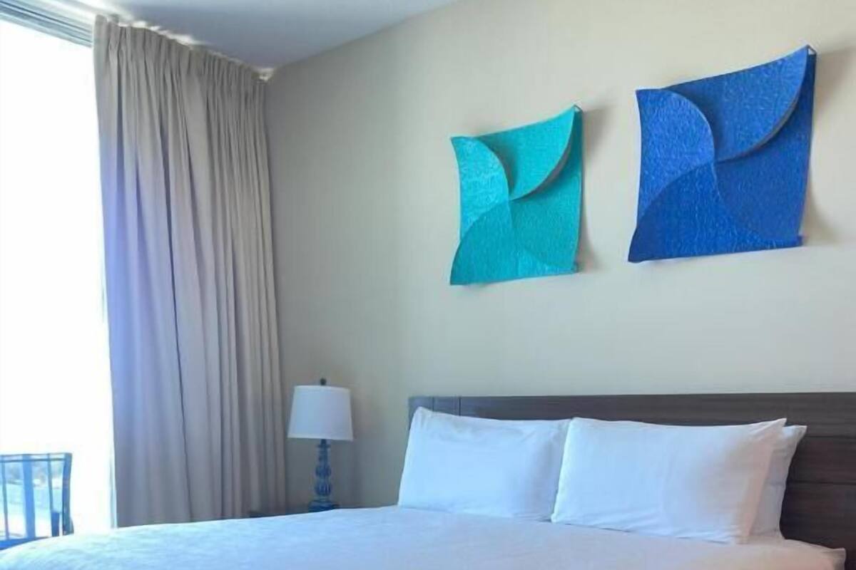 A hotel room with a large bed, a nightstand, a lamp, and two wall art pieces.
