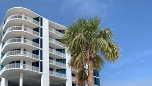 Un hotel de varios pisos con balcones, una palmera y una playa en primer plano.