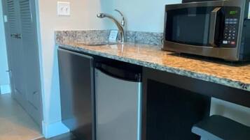 A compact kitchen with a built-in dishwasher, a microwave, and a small stool.