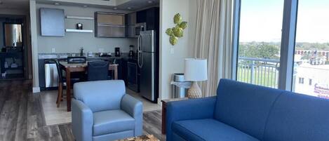 A modern hotel room with a living area, kitchenette, and a balcony with a view.