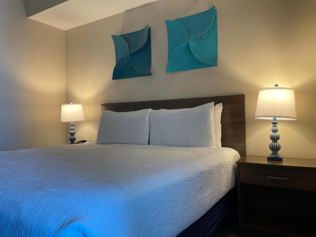 Un lit bien fait, avec du linge de lit blanc, deux œuvres d’art aux tons turquoise accrochées au mur et deux lampes de chevet posées sur des tables de nuit en bois.