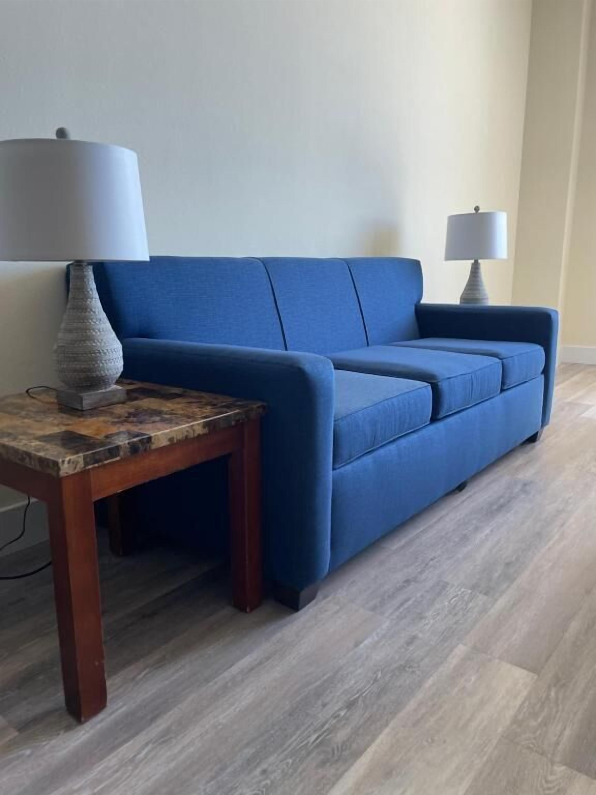 A room with a blue sofa, a wooden side table, and a lamp.