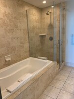 Um banheiro moderno com chuveiro em vidro, banheira branca e paredes com azulejos bege.