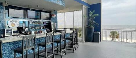 A bar area with a view of the ocean, featuring a counter with stools and a blue-tiled backsplash.