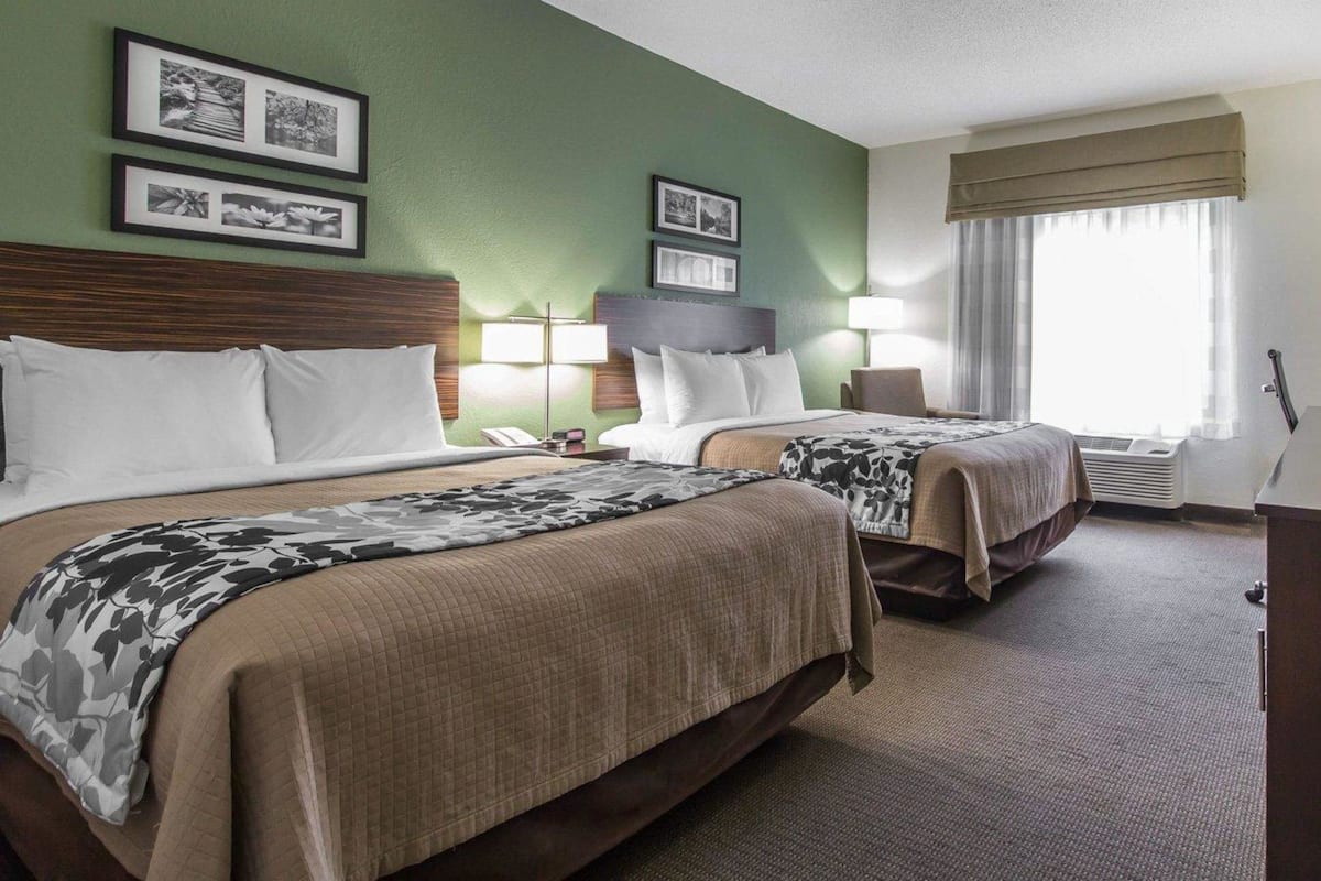 A hotel room with two beds, a green wall, framed pictures, a lamp, and a window with curtains.