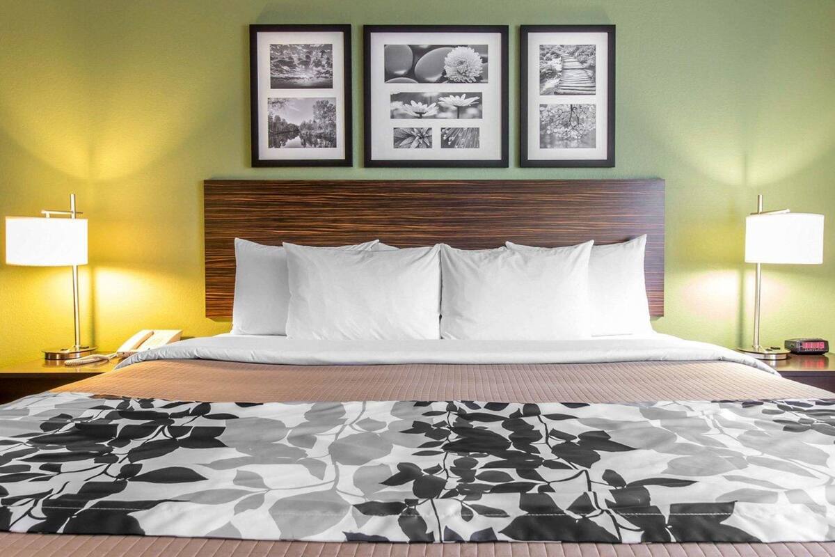 A hotel room with a bed, two bedside lamps, a nightstand, and three framed pictures on the wall.