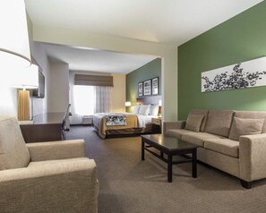 A hotel room with a sofa, a coffee table, a bed with a canopy, a TV, and artwork on the walls. - Sleep Inn & Suites Middlesboro (Middlesboro)