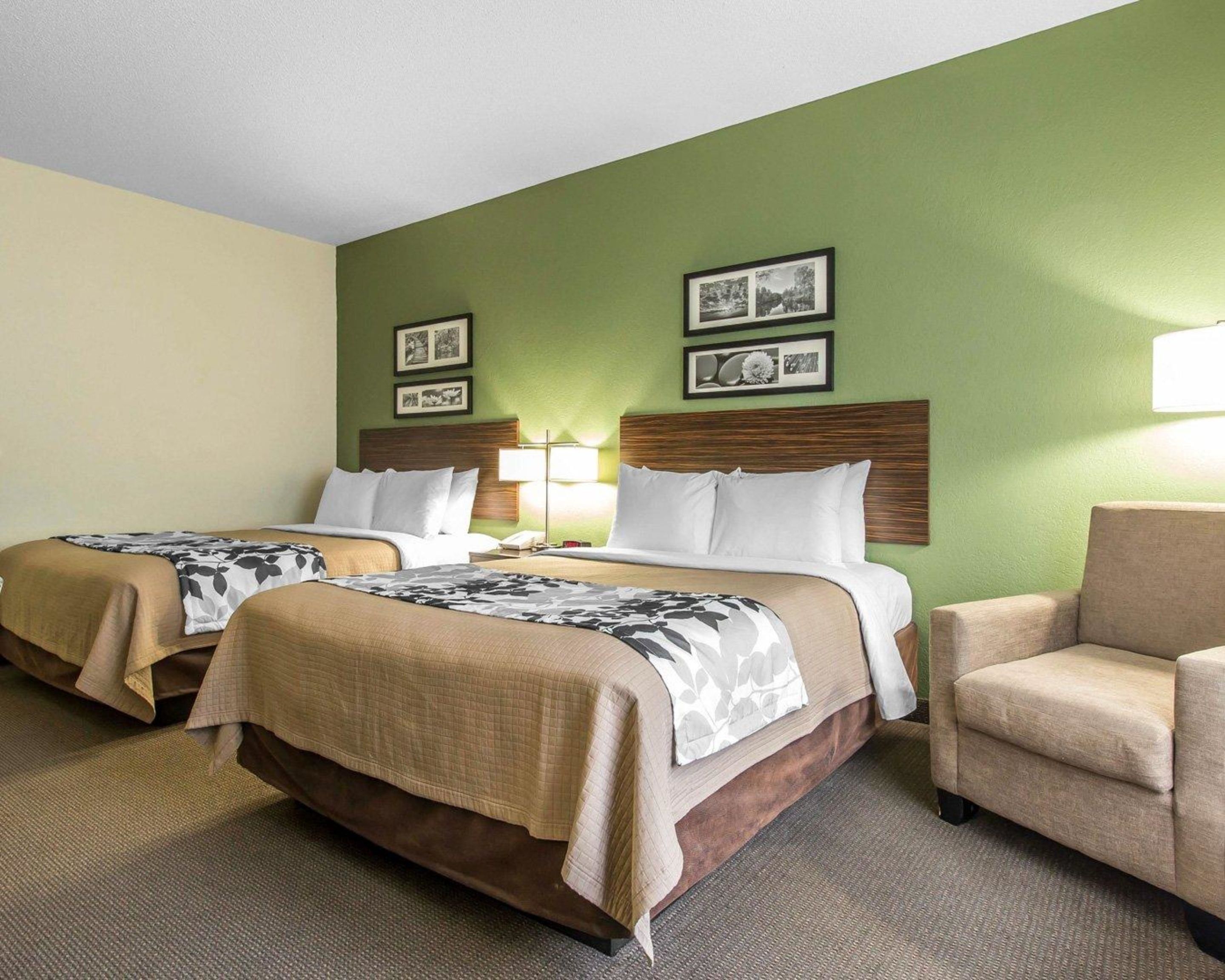 A hotel room with two beds, a chair, and a green wall.