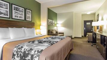 A hotel room with a large bed, a desk with a lamp, a chair, and a dresser.