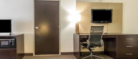 A hotel room with a desk, chair, TV, and a door.