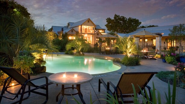 A poolside area with a house in the background, outdoor seating, and a well-lit evening setting. - Inn on Lake Granbury a Boutique Hotel (Granbury)