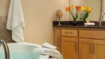 Un baño moderno con bañera, muebles de madera, encimera de granito, espejo y un florero con flores.
