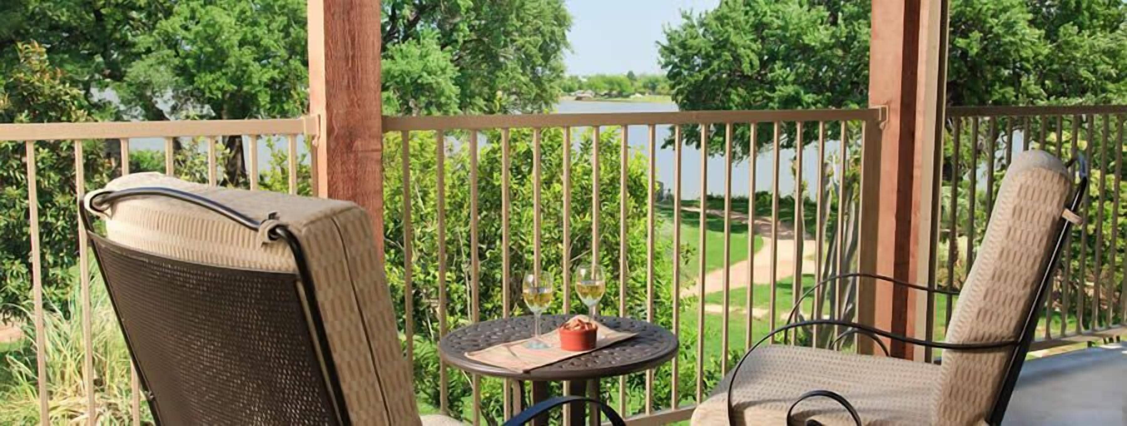 Un balcone con due sedie e un tavolino, con vista su un lago e vegetazione.
