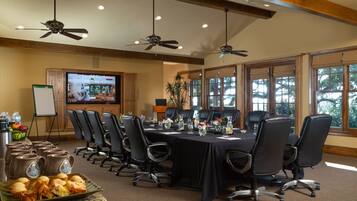 A conference room with a long table, multiple chairs, ceiling fans, a large screen, and a buffet table with food.