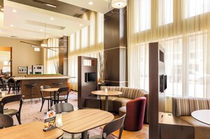 A modern hotel lobby with a bar area, seating arrangements, and large windows allowing natural light.
