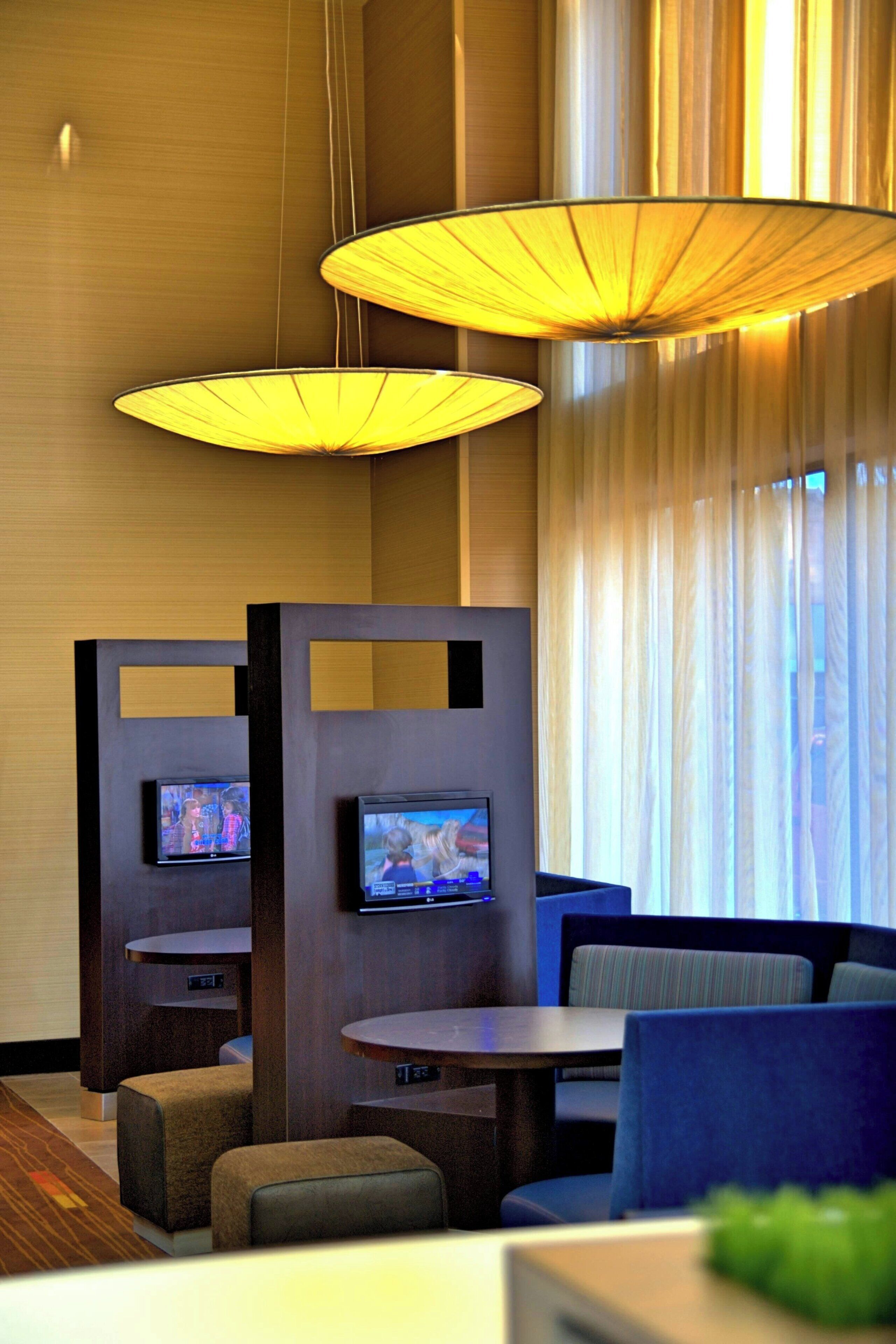 A modern hotel lobby with seating areas, television screens, and large hanging lamps.