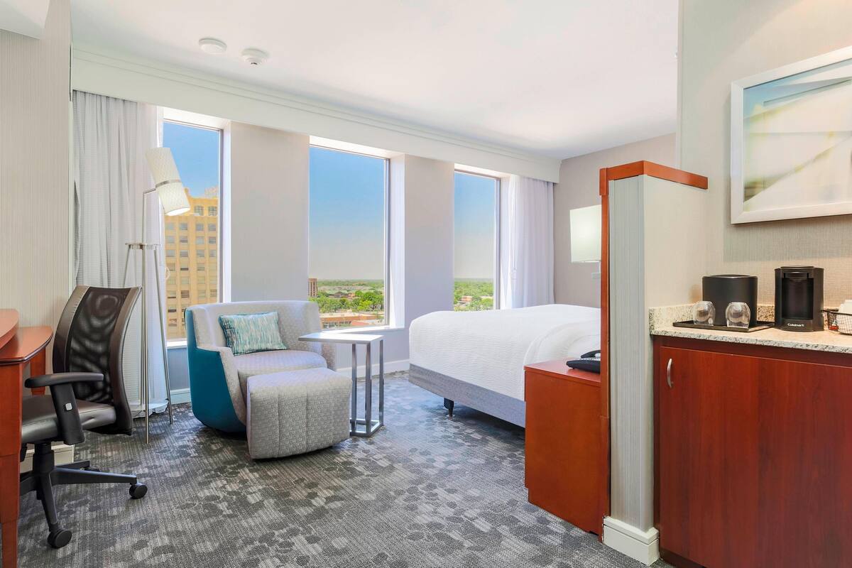 A hotel room with a bed, a desk, a chair, a small table, and a sofa.