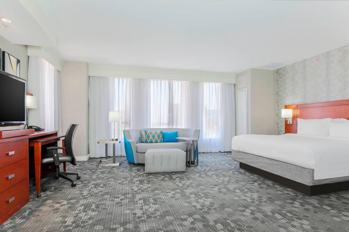 A hotel room with a bed, a desk with a computer, a chair, a sofa, and a TV.