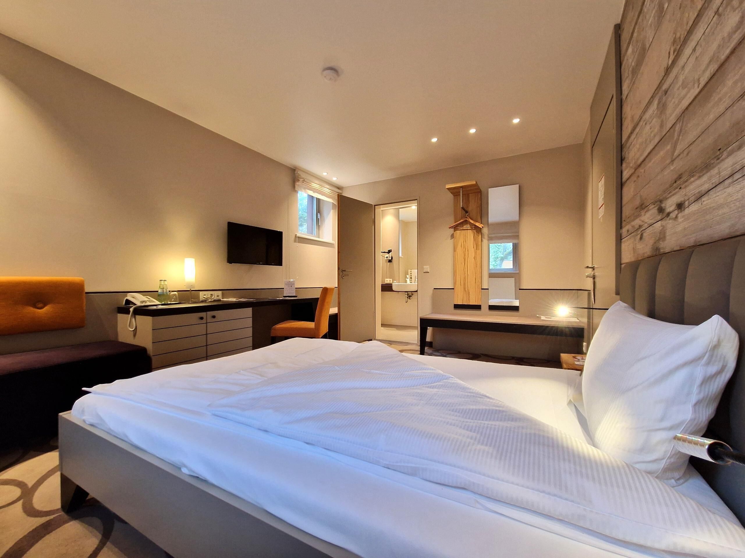 A modern bedroom with a large bed, a desk, a chair, and a TV.
