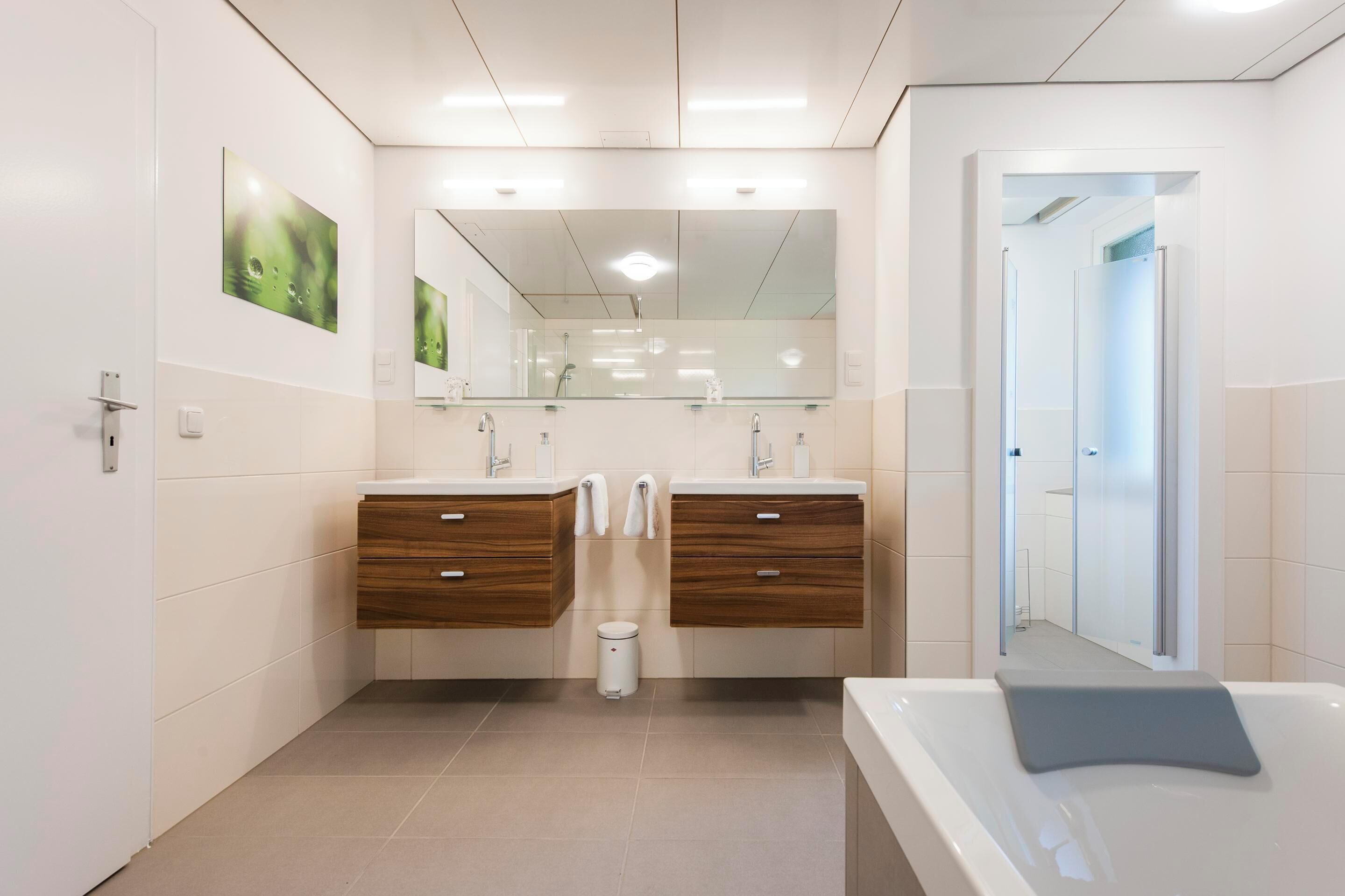 Un baño moderno con dos lavamanos, un espejo grande y una bañera.