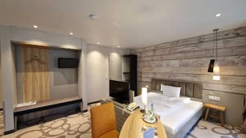 A modern hotel room with a bed, a desk with a chair, a TV, a wooden wardrobe, and a wooden wall panel.