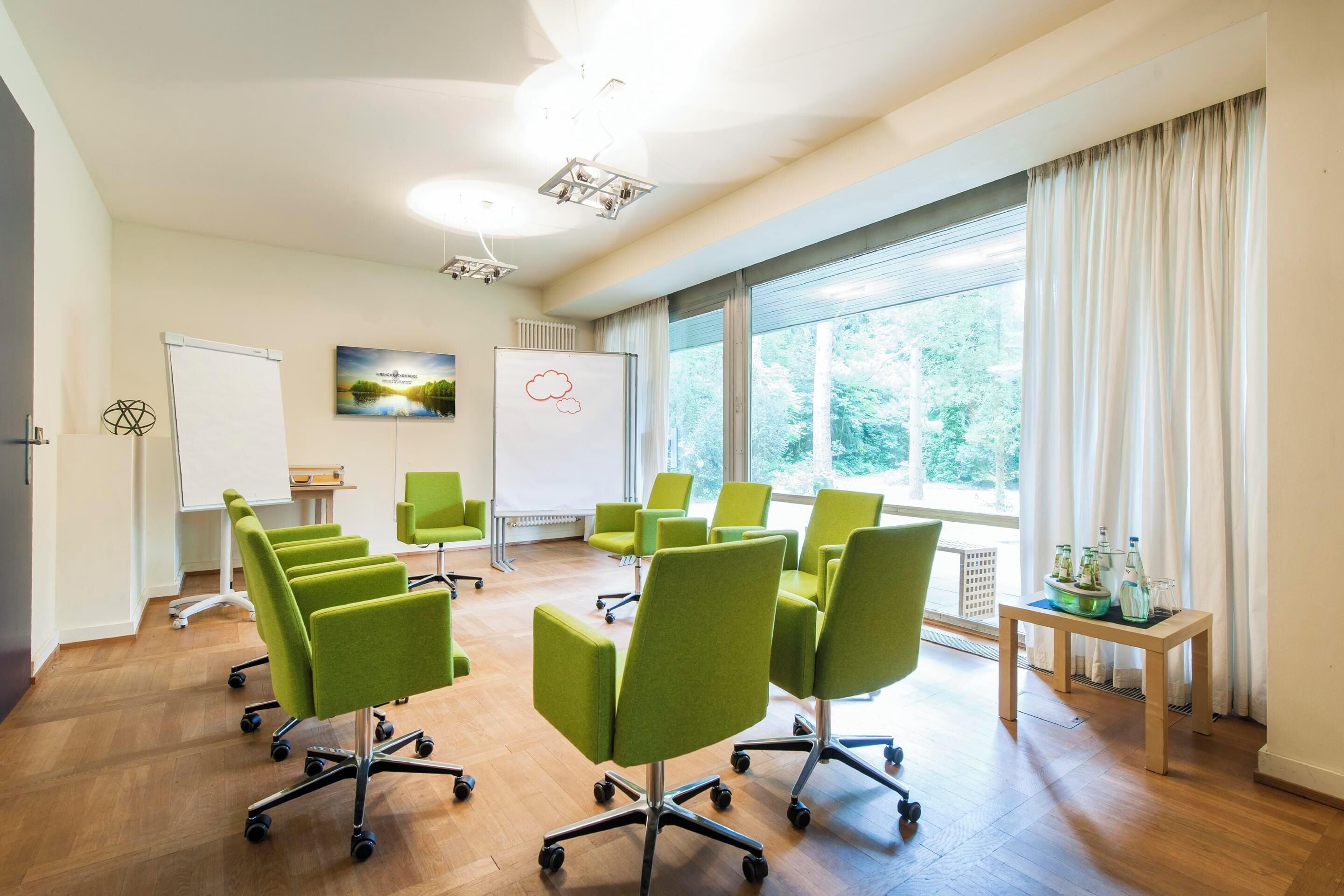 Un salón de conferencias con sillas verdes, una pizarra y una mesa con adornos.