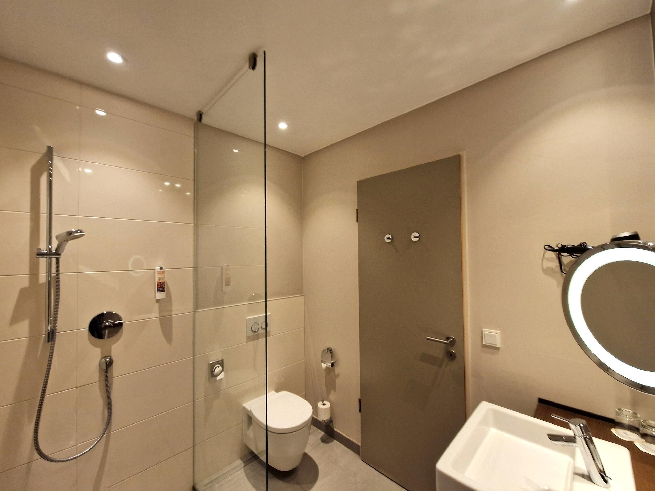 A modern bathroom with a glass shower enclosure, a toilet, a sink with a mirror, and a door with a handle.