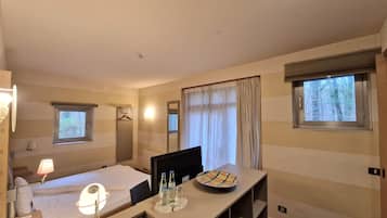 A hotel room with a bed, a desk with a plate and bottles, a mirror, and two windows.