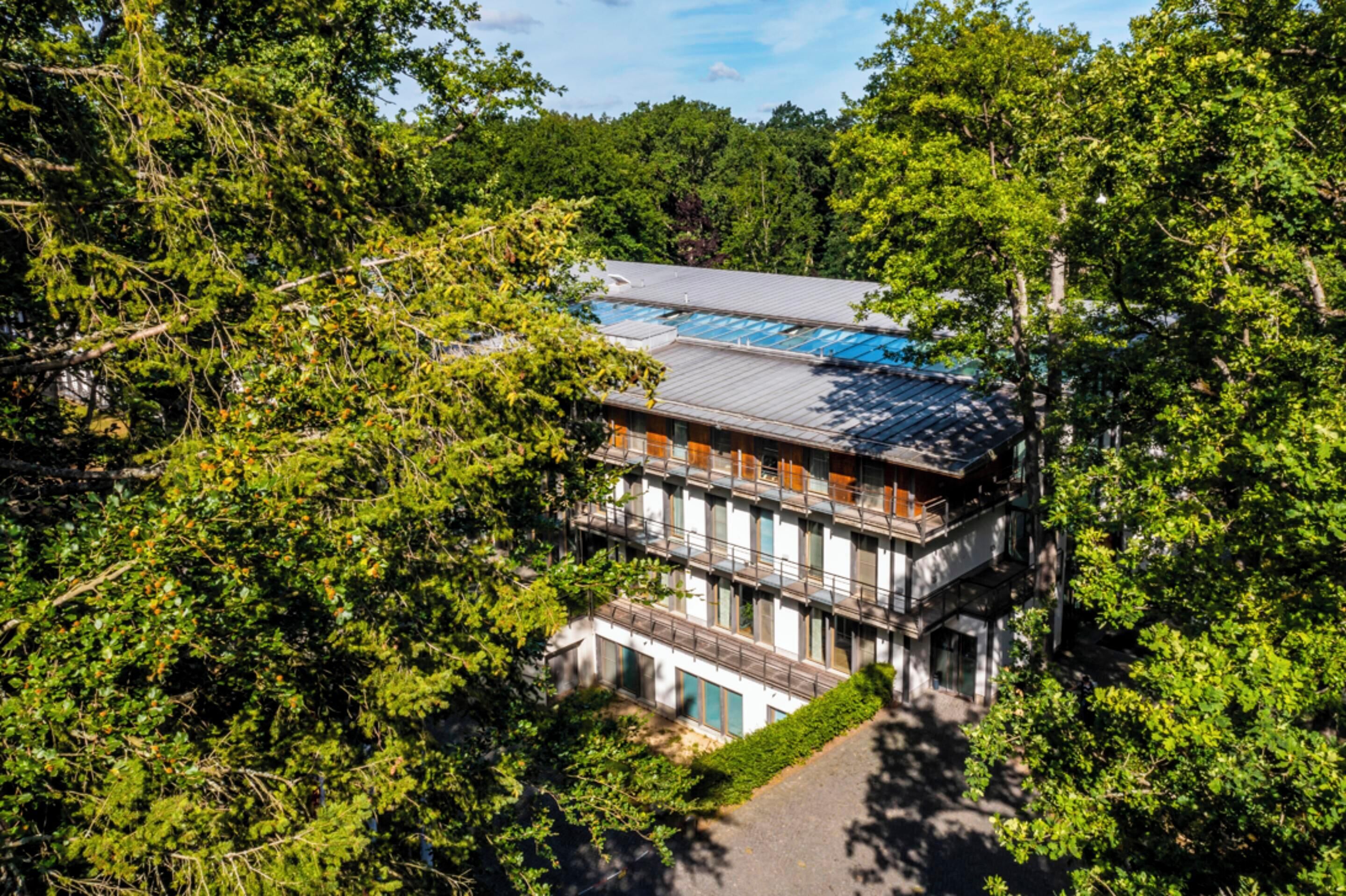 A multi-story building with a flat roof, surrounded by dense greenery.