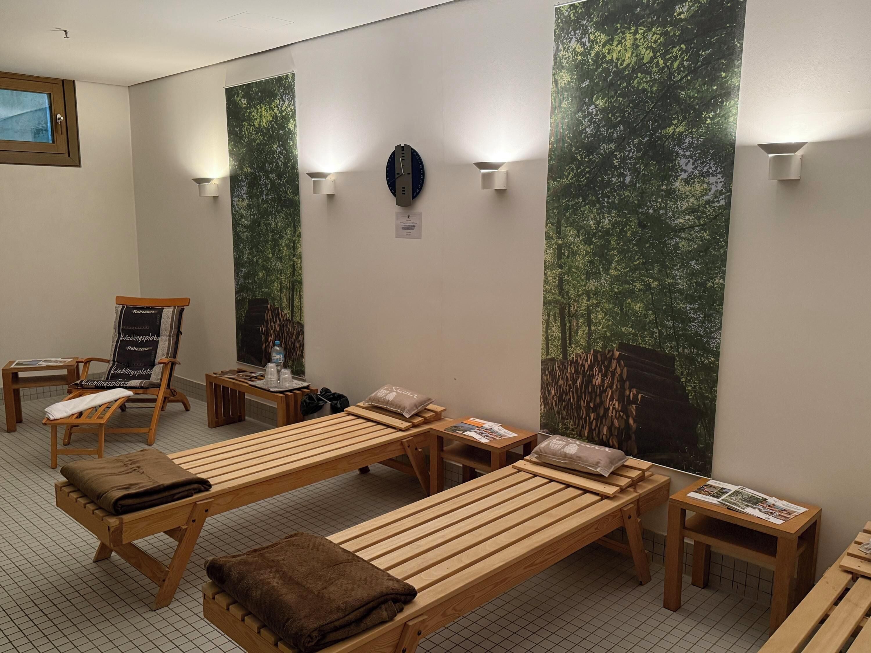 A sauna room with wooden benches, towels, and a poster of a forest scene.
