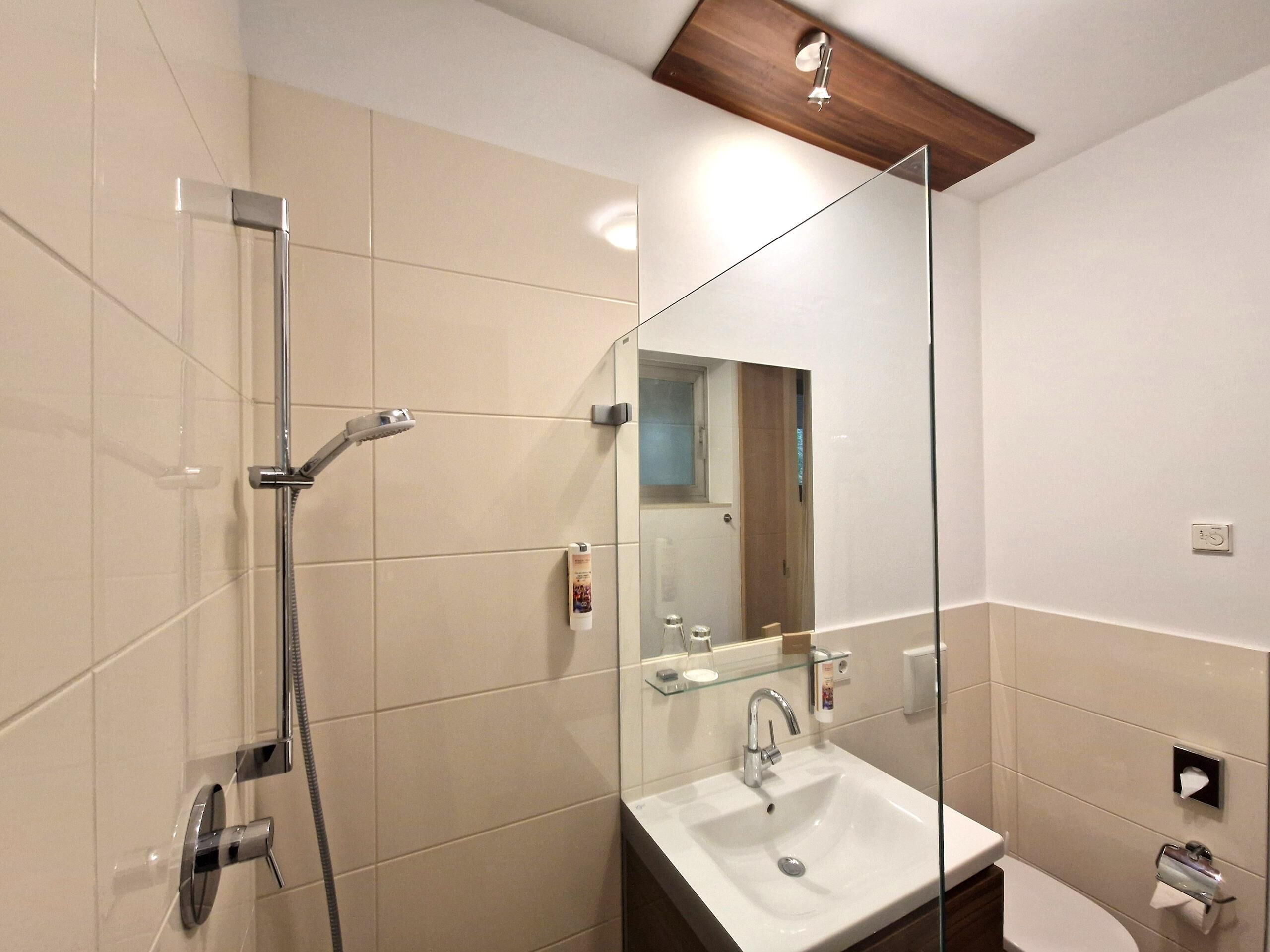 Ein modernes Badezimmer mit Duschkabine aus Glas, Waschbecken mit Spiegel und Holzboden.
