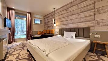 Una habitación de hotel moderna con una cama grande, un panel de madera decorativo, un escritorio pequeño y una ventana con cortinas.