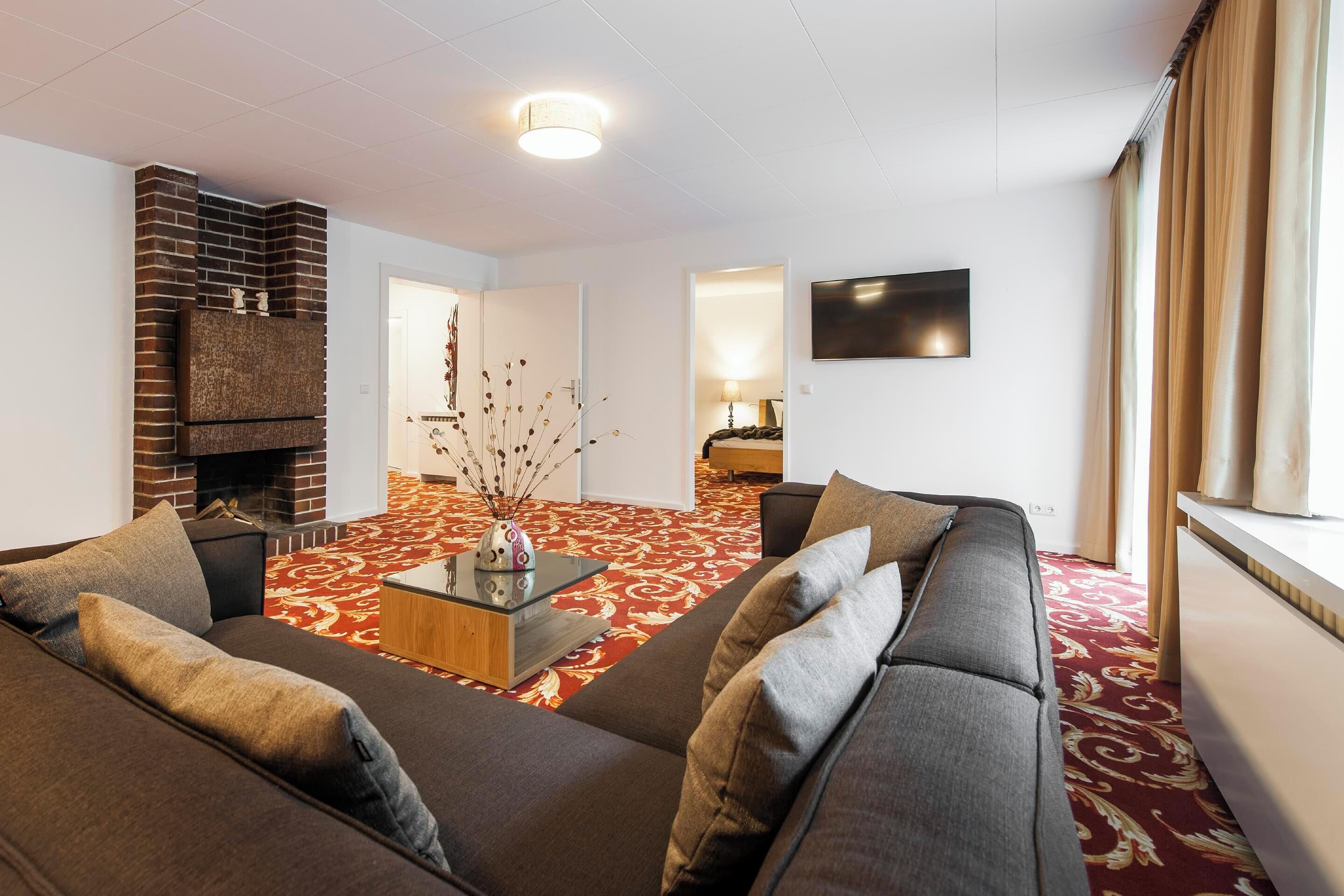 Ein modernes Wohnzimmer mit Kamin, einer Sofagarnitur, einem Couchtisch und einem gemusterten Teppich.
