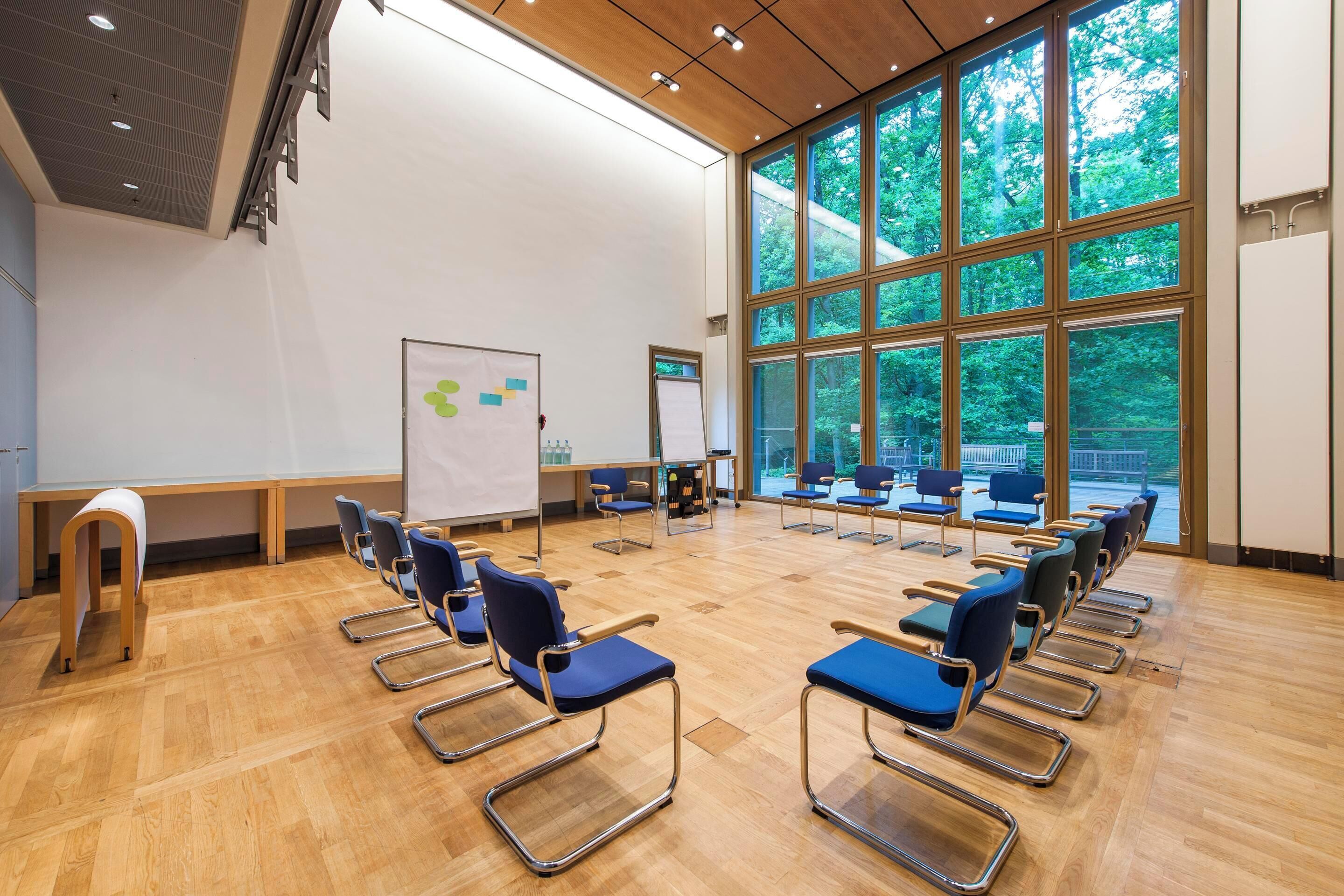 Uma sala de conferências com quadro branco, cadeiras azuis e janelas amplas.