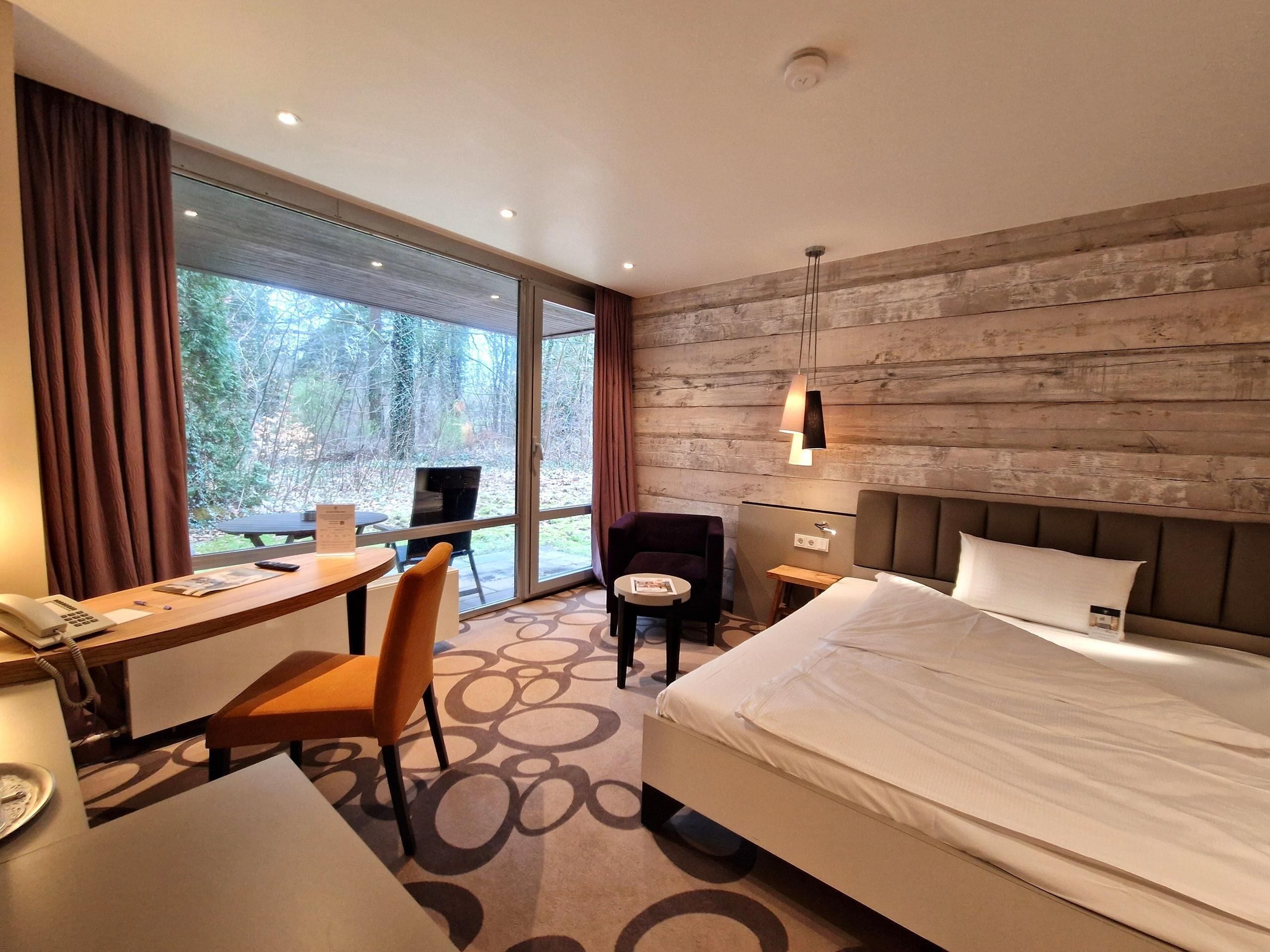 A hotel room with a bed, desk, chair, and a view of the outdoors.