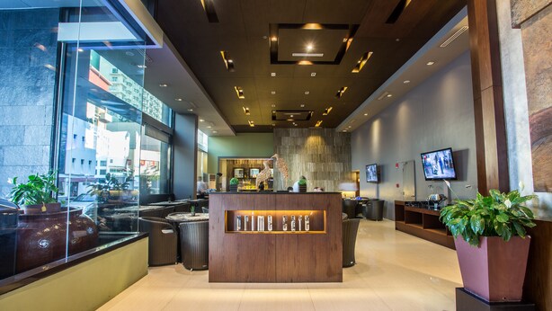 A modern lobby with a reception desk, seating area, and large windows overlooking the street. - The B Hotel (Muntinlupa)