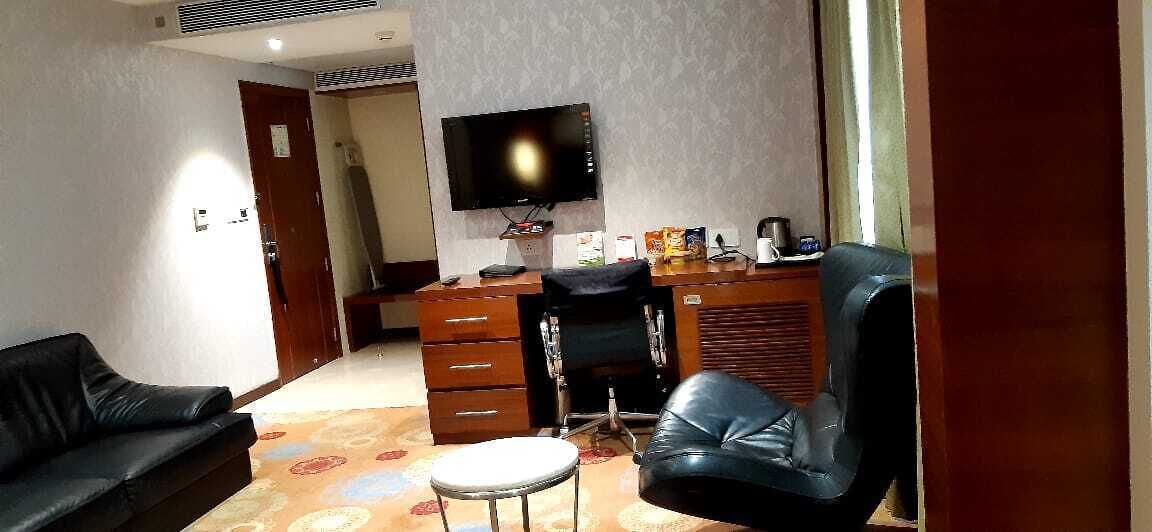 A hotel room with a black leather sofa, a black leather chair, a small round table, a desk with a computer and a flat-screen TV, and a patterned carpet.