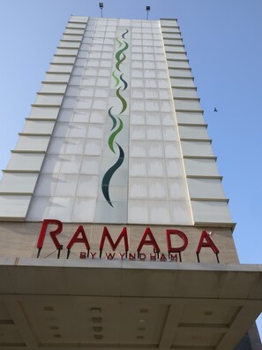 Un immeuble imposant, doté d’une architecture moderne, avec un logo bien visible et le nom « RAMADA » inscrit à sa base.