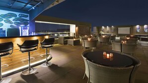 Ein Außenbereich mit Bar, hochgestellten Barhocker, einer Theke und einer Lounge mit runden Tischen und Stühlen.