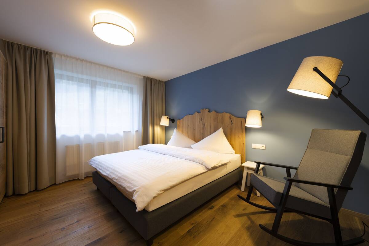 Un lit bien fait, avec du linge de lit blanc, une tête de lit en bois et une table de chevet avec une lampe.