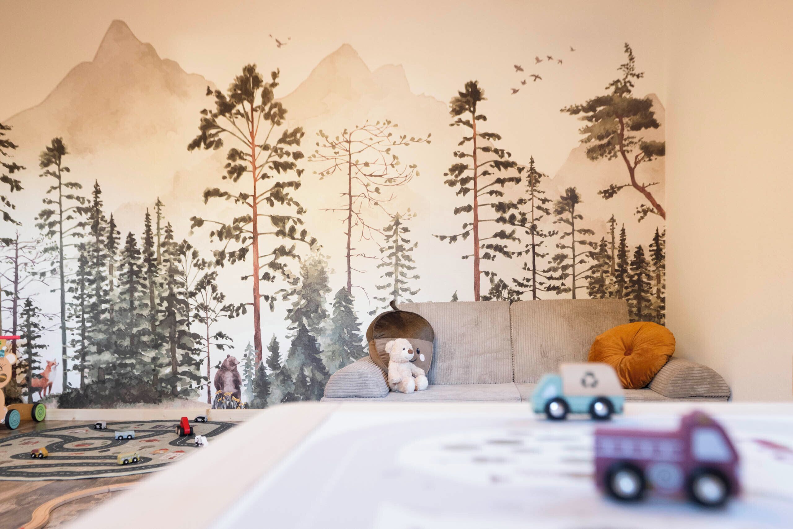 A play area with a mountain mural, a sofa, a teddy bear, and toy vehicles.