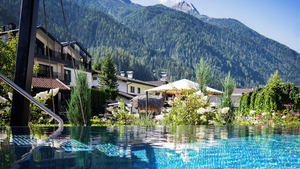 Ein Schwimmbecken mit Bergblick, umgeben von Gebäuden mit Balkonen und einem Blumenblütengarten.