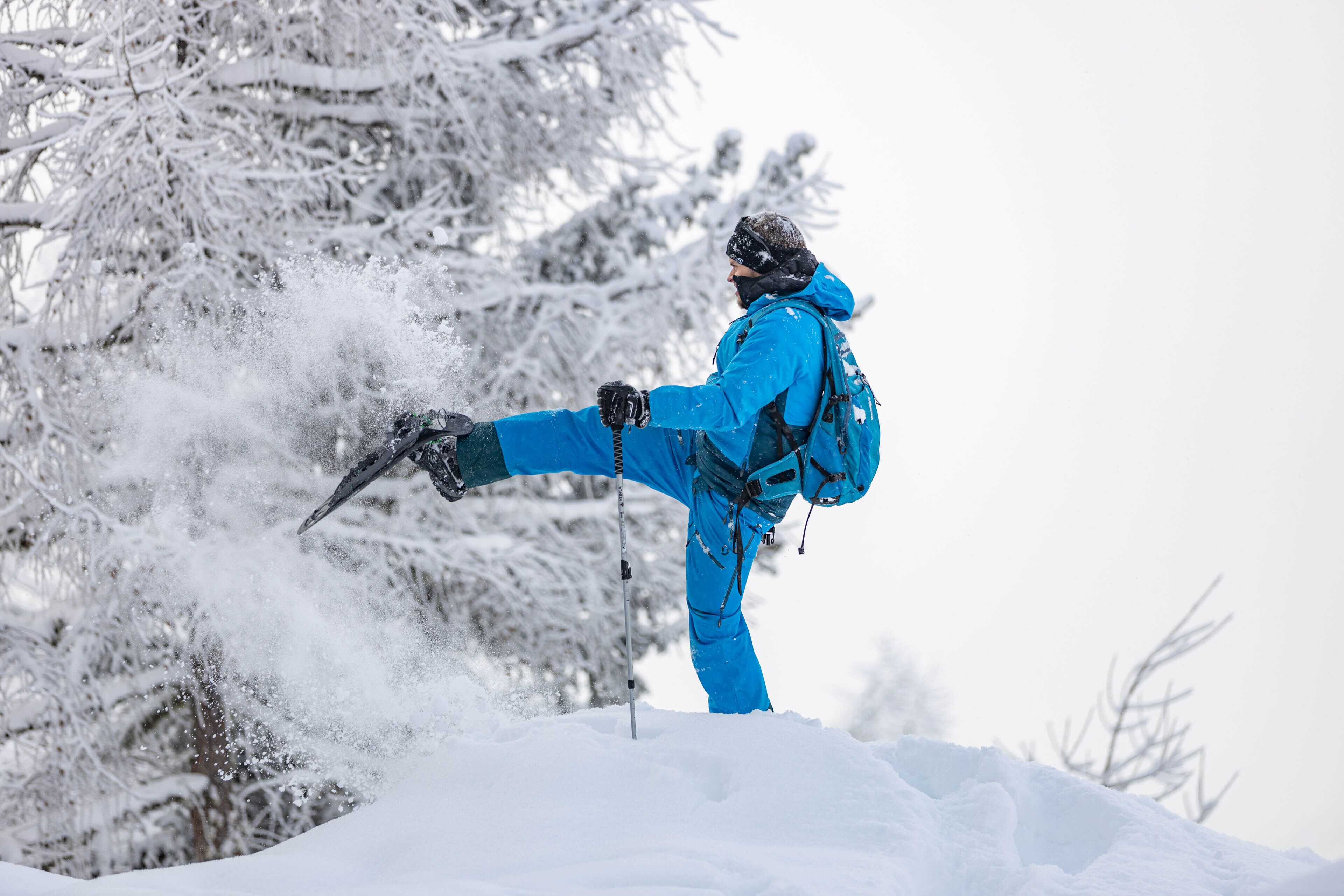 Uma pessoa vestida com roupas de inverno em azul, em meio à neve, com uma prancha de snowboard.