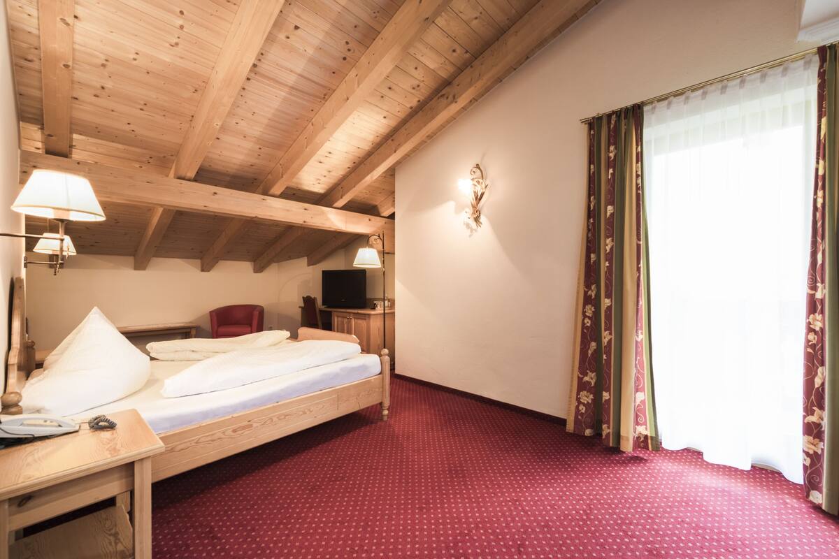 Une chambre d’hôtel avec un plafond en bois, un lit avec une literie blanche, un bureau avec une lampe, une chaise et un téléviseur.