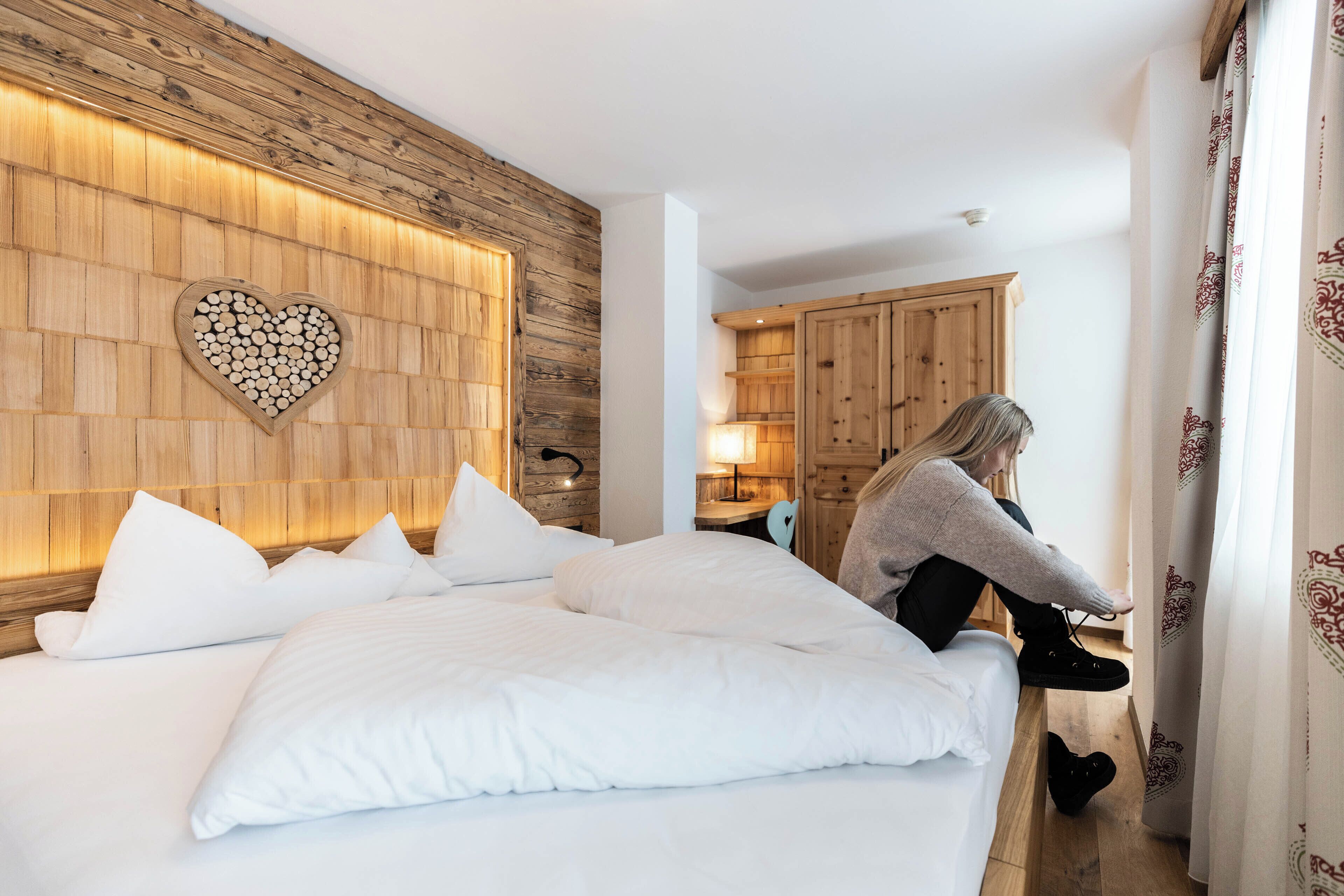 A bedroom with a wooden headboard, a heart-shaped wall decoration, and a person sitting by the bed.