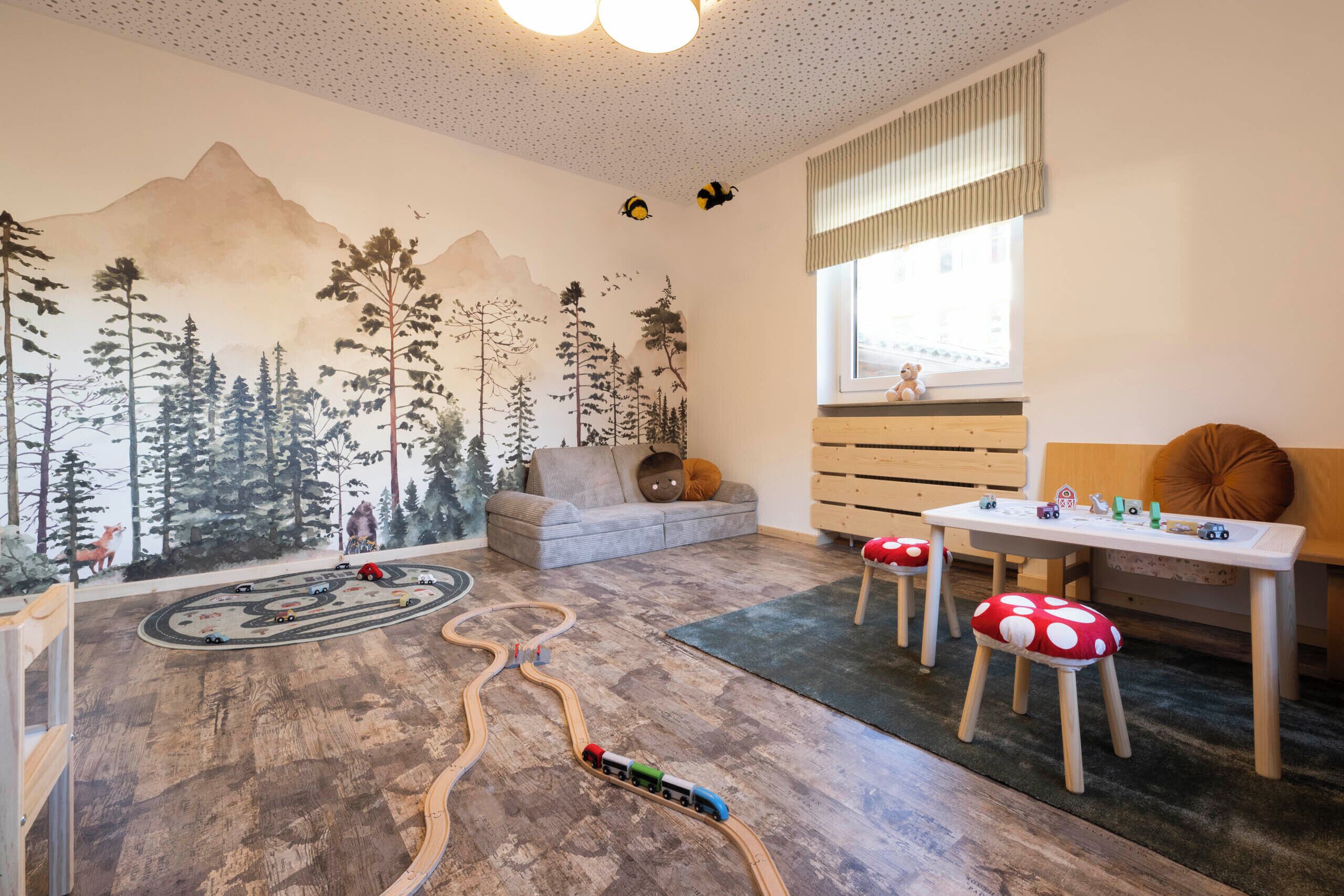 Un cuarto infantil con una disposición de vías de tren, un mural de un bosque y una ventana con vistas.